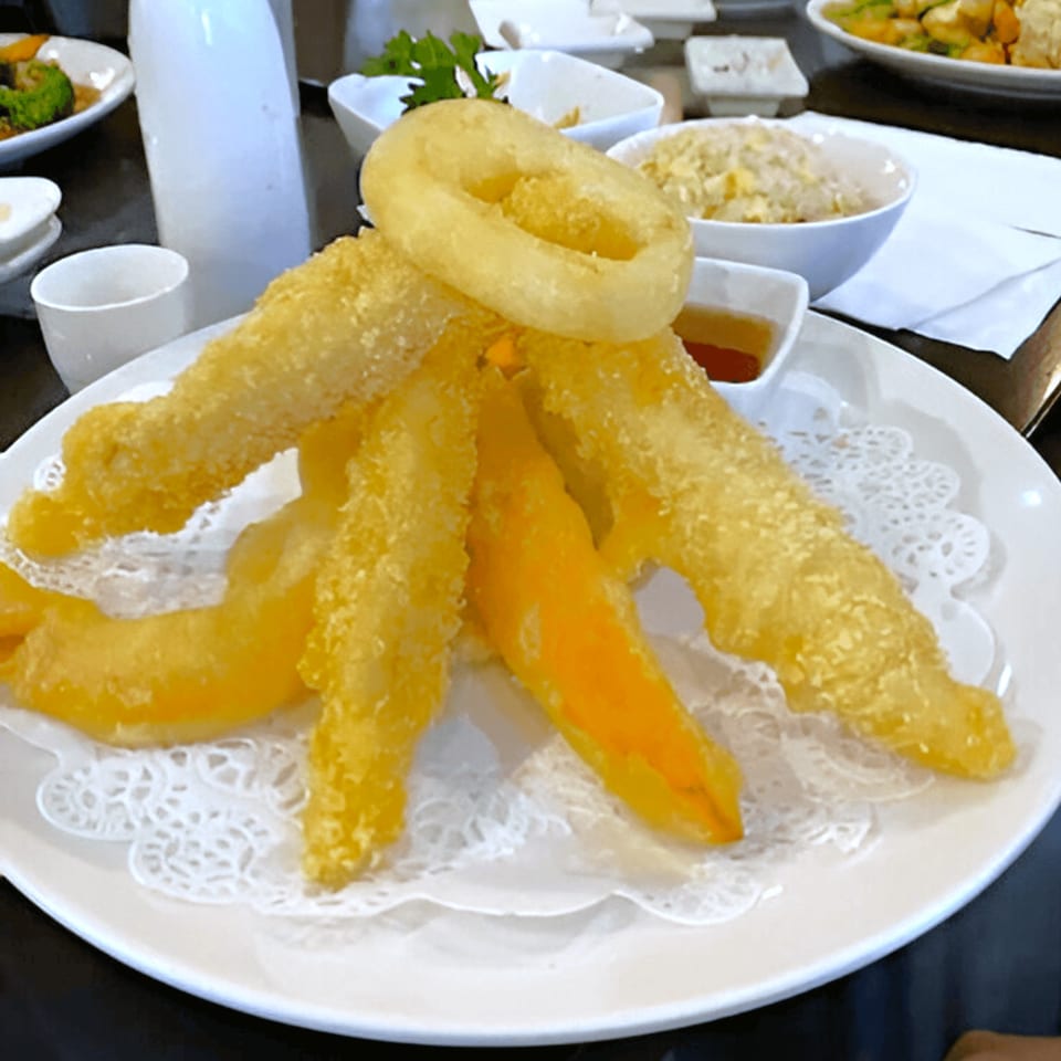 Golden tempura shrimp, sweet potato, and onion rings on a white plate with dipping sauce.