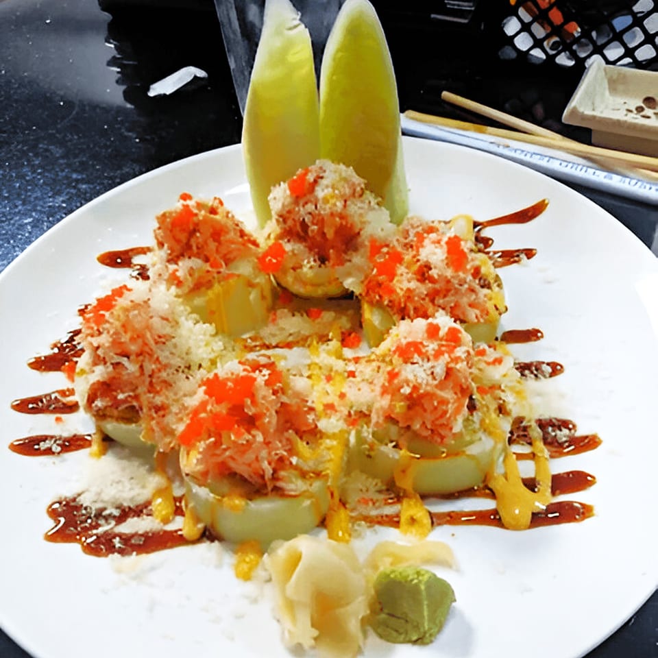 Corner Sushi's special roll with crab, roe, sauce, and two lime wedges on a white plate.