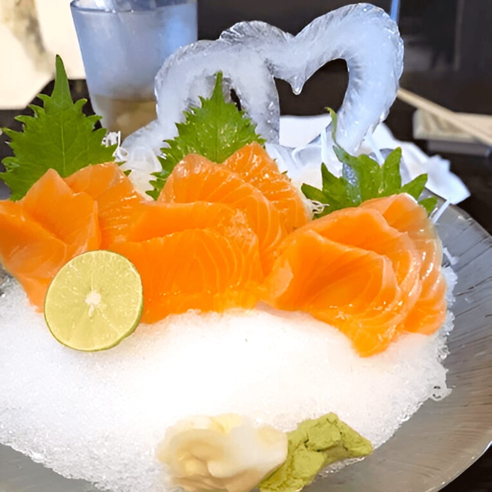 Fresh salmon sashimi with a lime slice, ginger, wasabi, and an ice sculpture on a bed of ice.