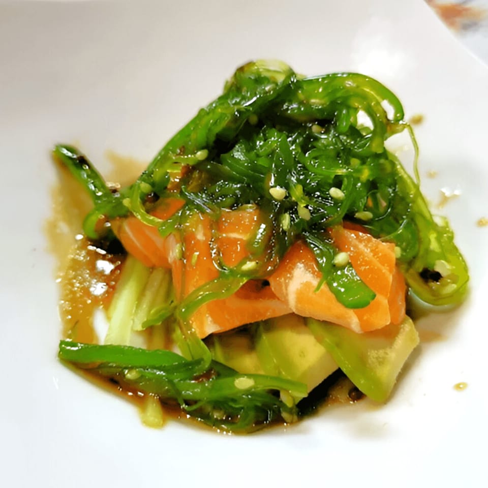 Salmon and avocado salad topped with bright green seaweed and sesame seeds.