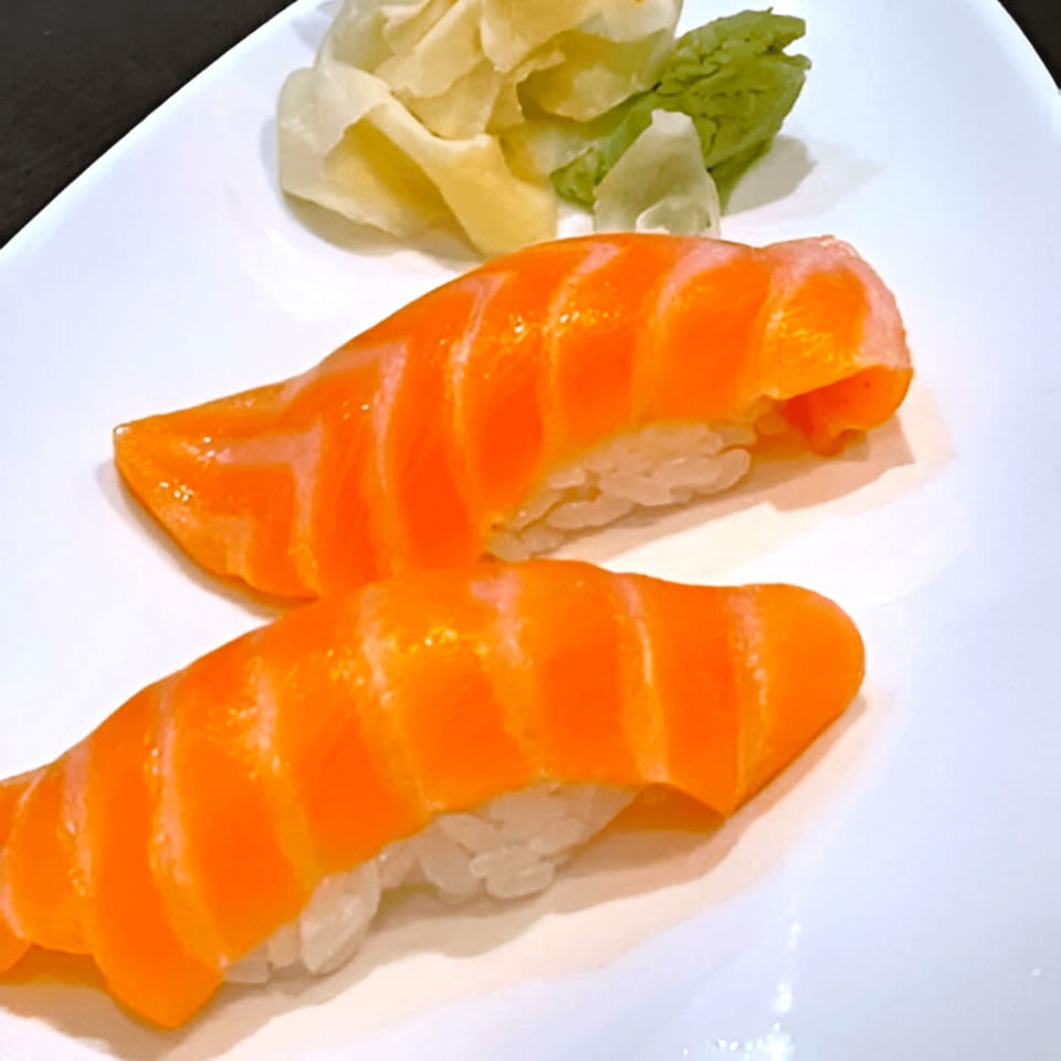 Two pieces of salmon nigiri sushi with ginger and wasabi on a white plate.